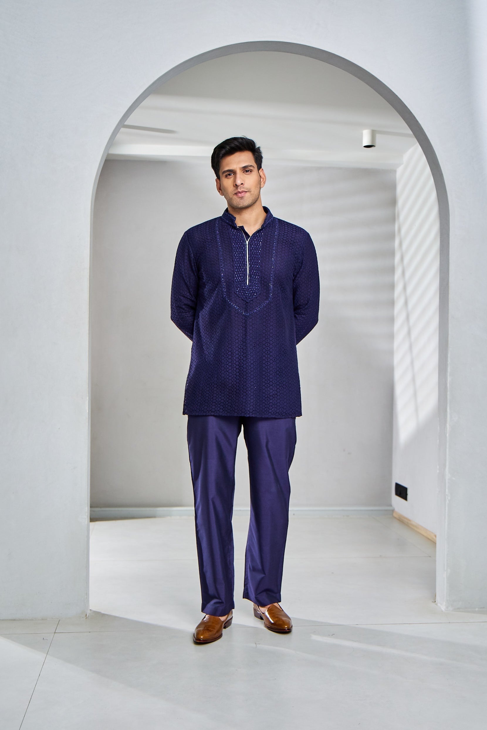 A man poses in a navy blue short kurta, featuring cotton fabric with Lucknowi and crochet embroidery on the neckline and sleeves.