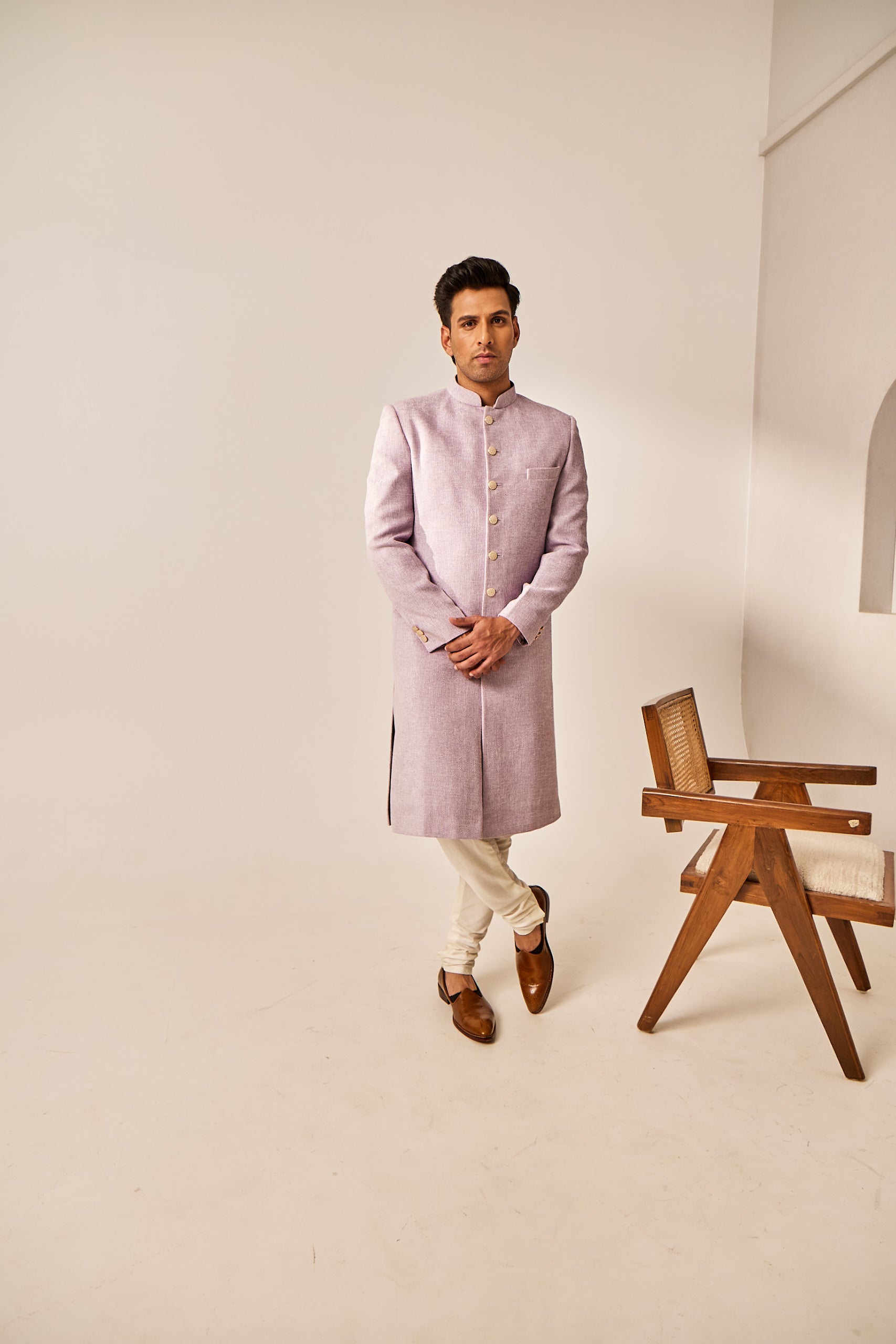 A man poses in a purple Jude silk sherwani with antique buttons, paired with a matching churidar for a timeless, traditional look.