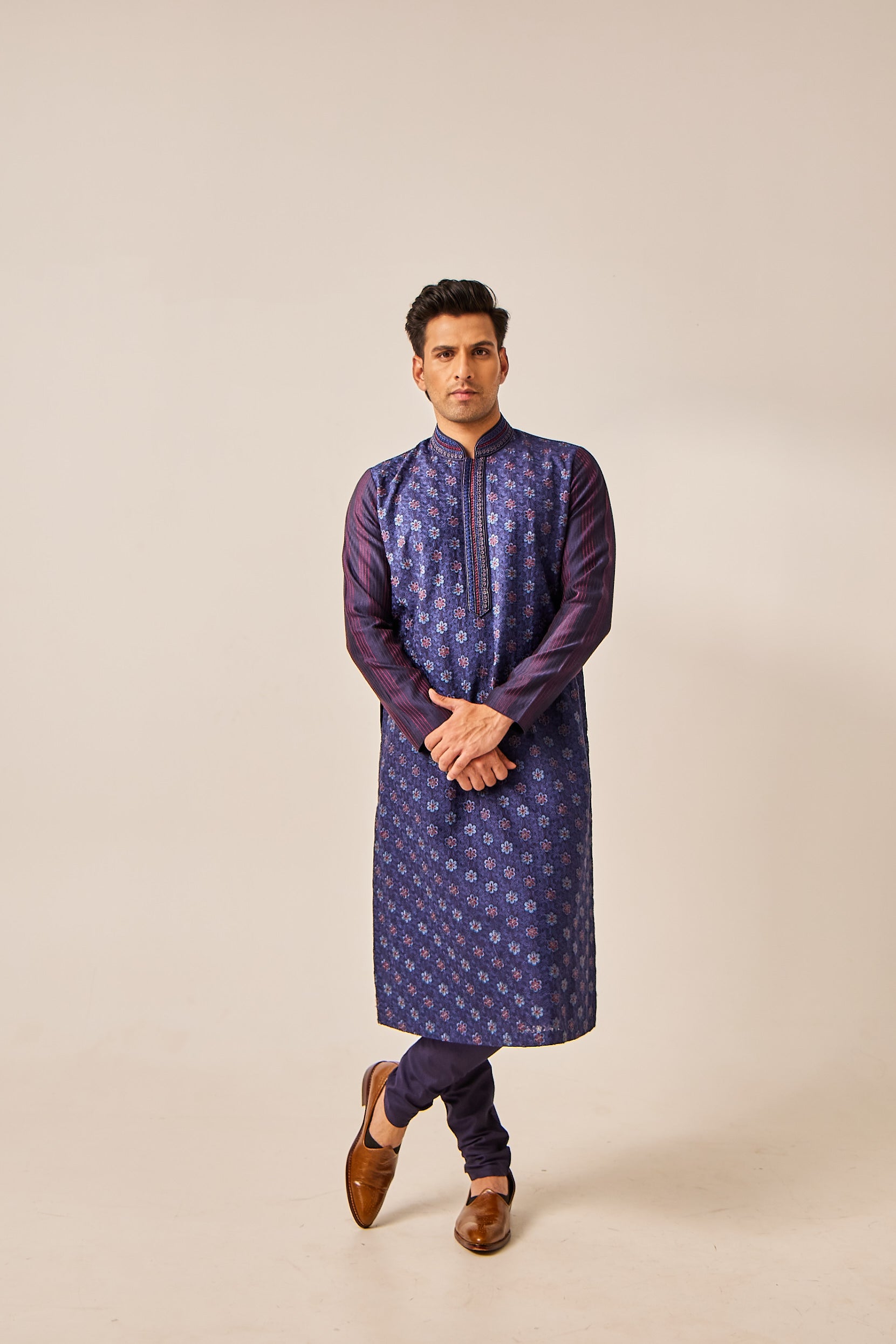 A man poses in a blue Chanderi silk kurta embellished with resham thread work and moti detailing, paired with a matching cotton silk churidar for a refined traditional look.
