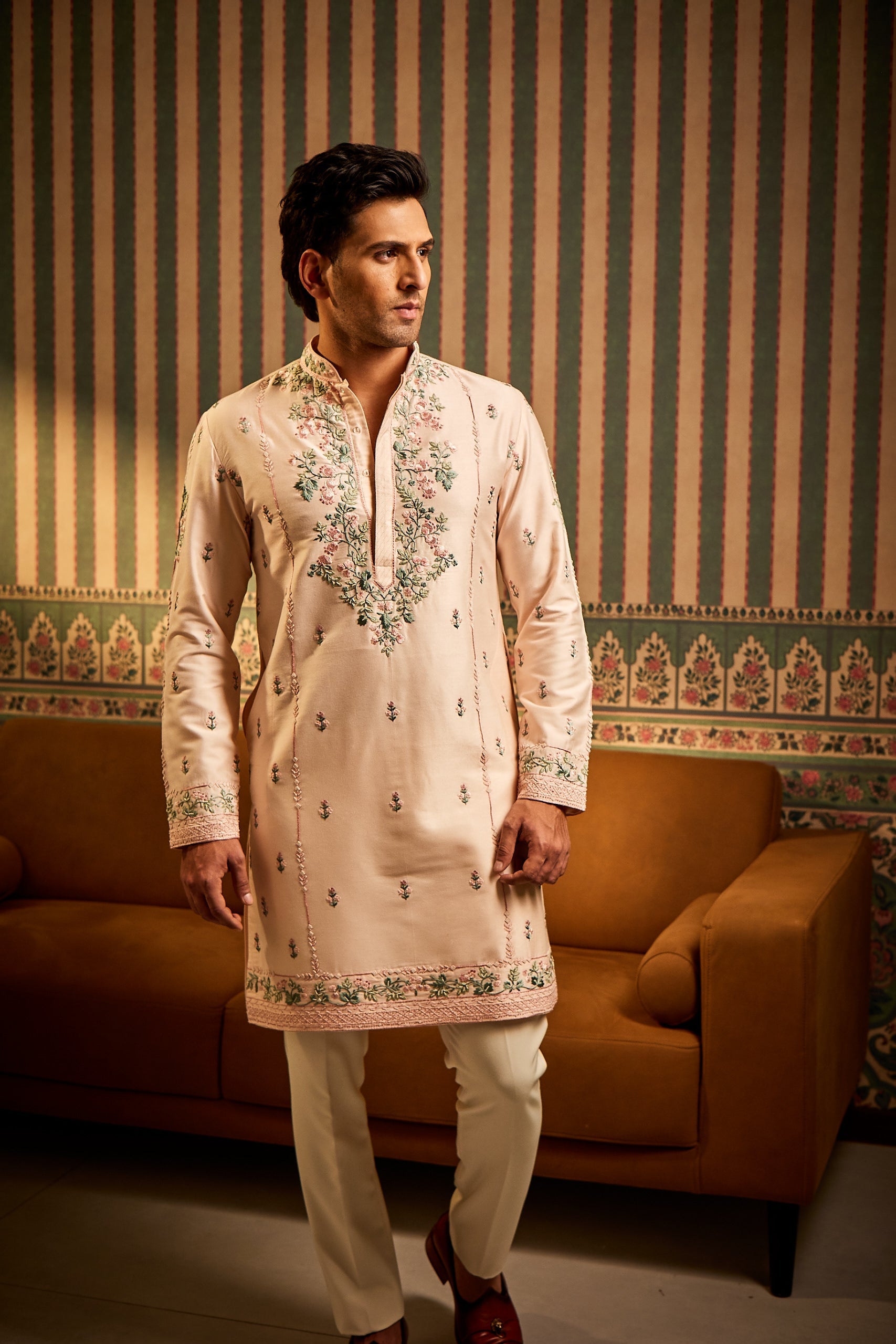 A man poses in a pink cotton silk kurta featuring hand-embroidered multi-color resham thread work on the front and sleeves, paired with an Ali Ghadi trouser and churidar for a vibrant traditional look.
