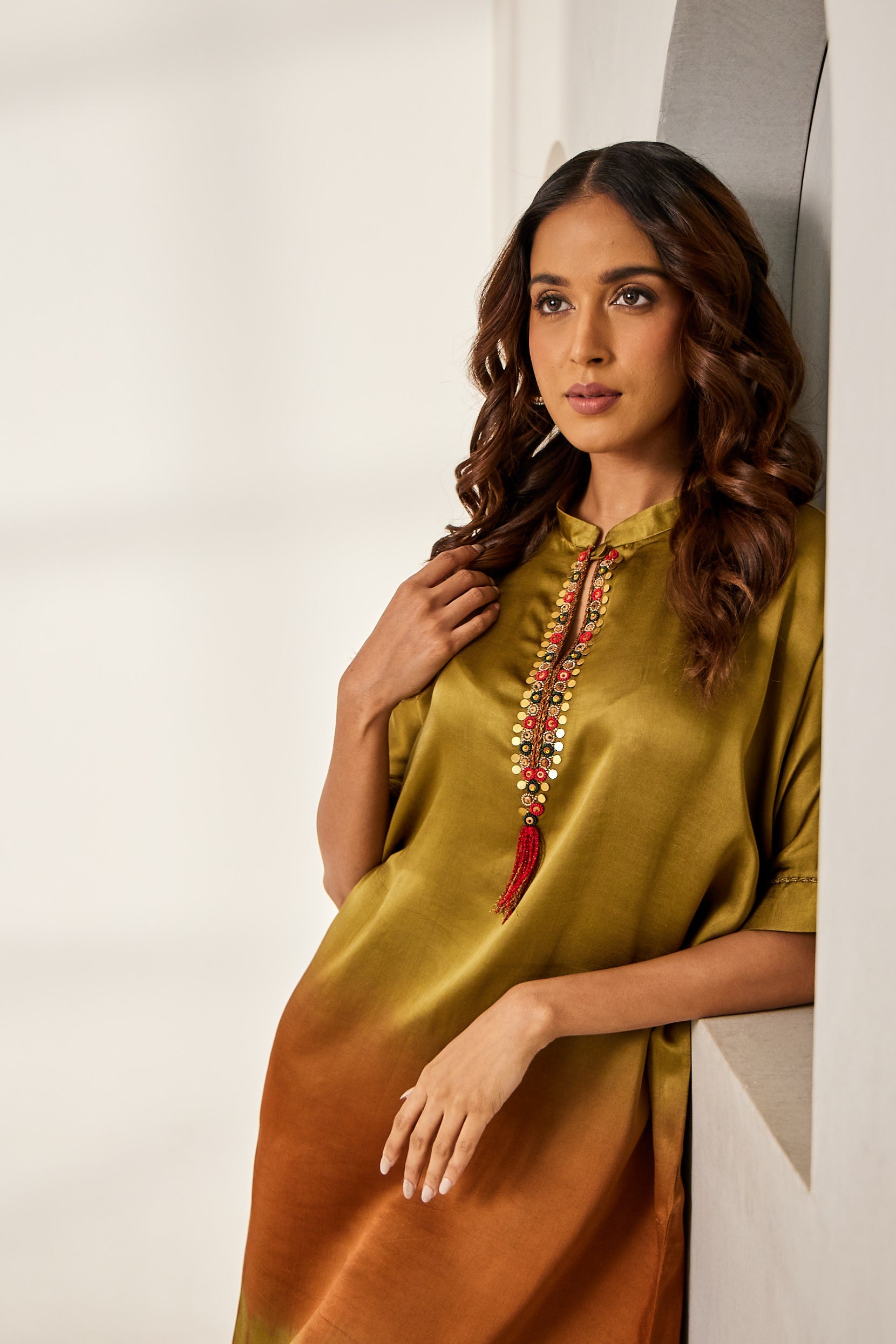 A woman poses in a mustard green and rust tie-dyed kurti from BenzerWorld as she leans against a wall.
