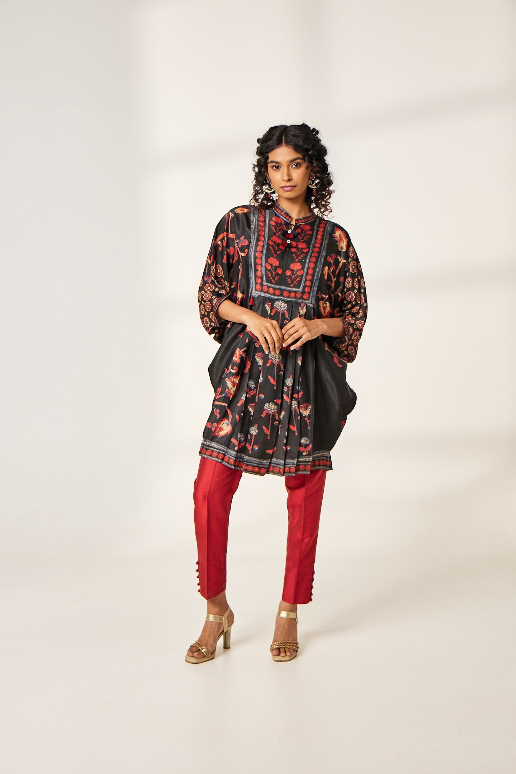 A woman poses in a black silk kaftan-style kurti with a red floral print from BenzerWorld.