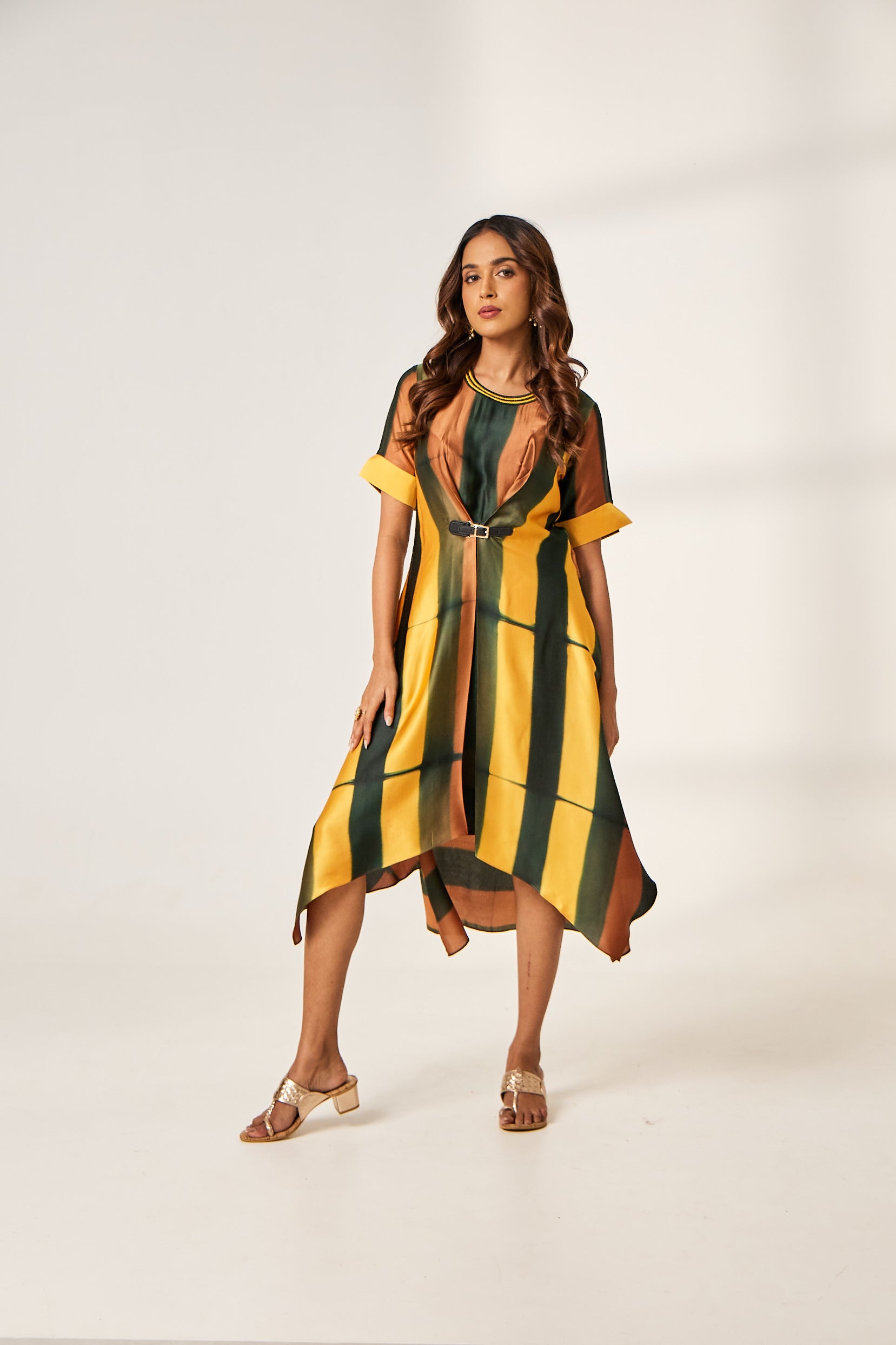 A woman poses in a yellow, olive green, and rust coloured tie-dyed kurti from BenzerWorld with an accompanying leather belt.