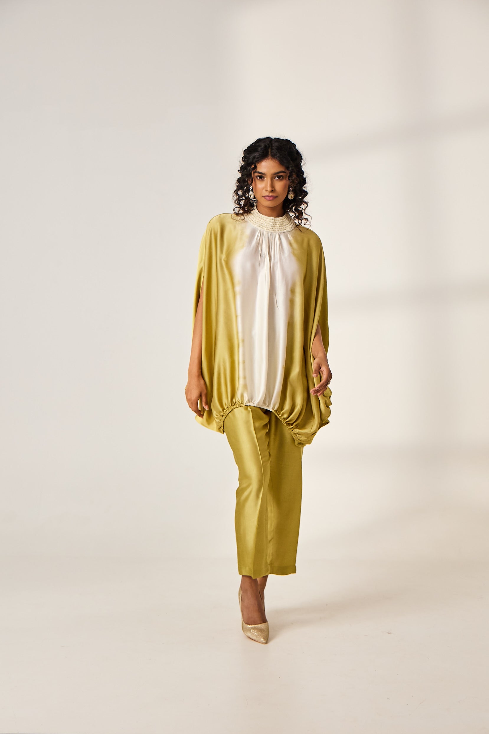 A woman poses in a satin co-ord set from Benzer which includes a white and green tie-dyed cape top with green straight pants.