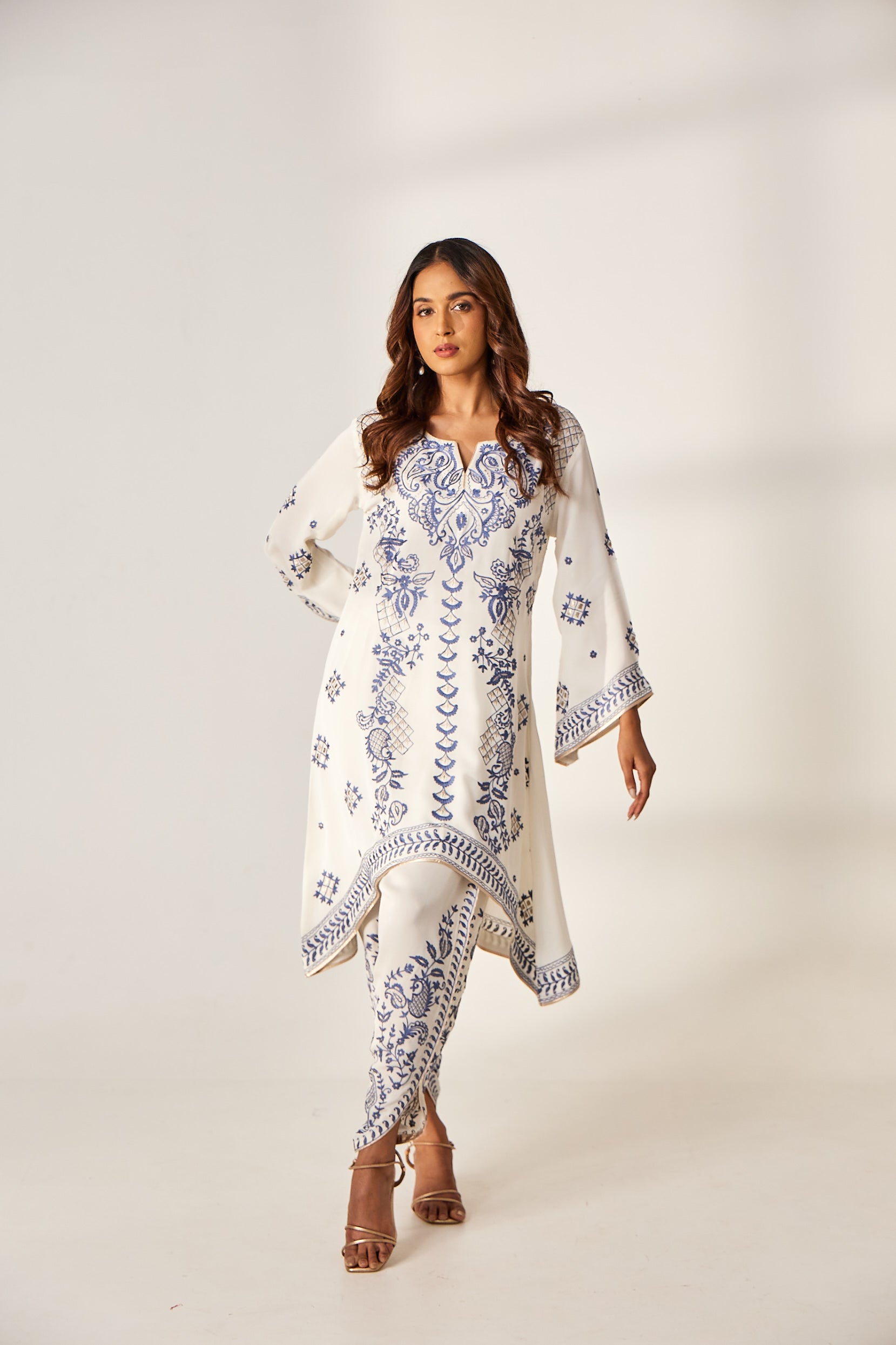 A woman poses in a white georgette co-ord set which includes a V-cut kurta with resham thread work and a dhoti-style pant.