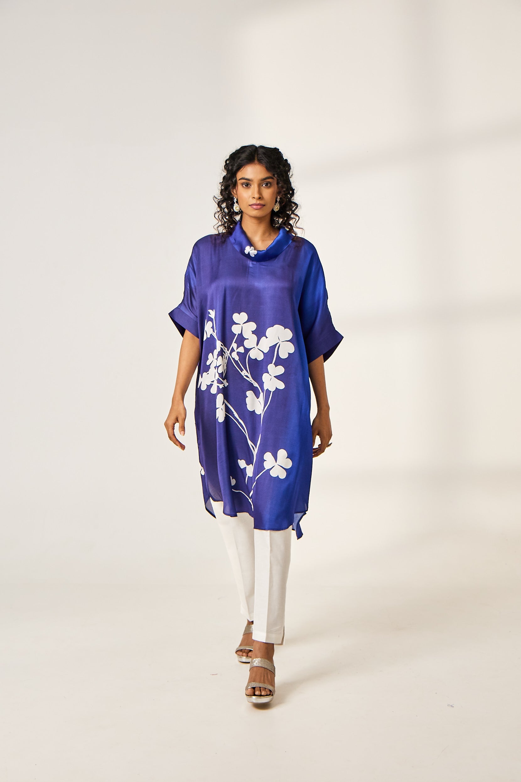 A woman poses in an Indowestern kaftan tunic in soft pastel hues, featuring flowing georgette fabric with intricate thread and mirror embroidery along the neckline and borders, styled with slim-fit trousers and statement earrings for a contemporary ethnic look
