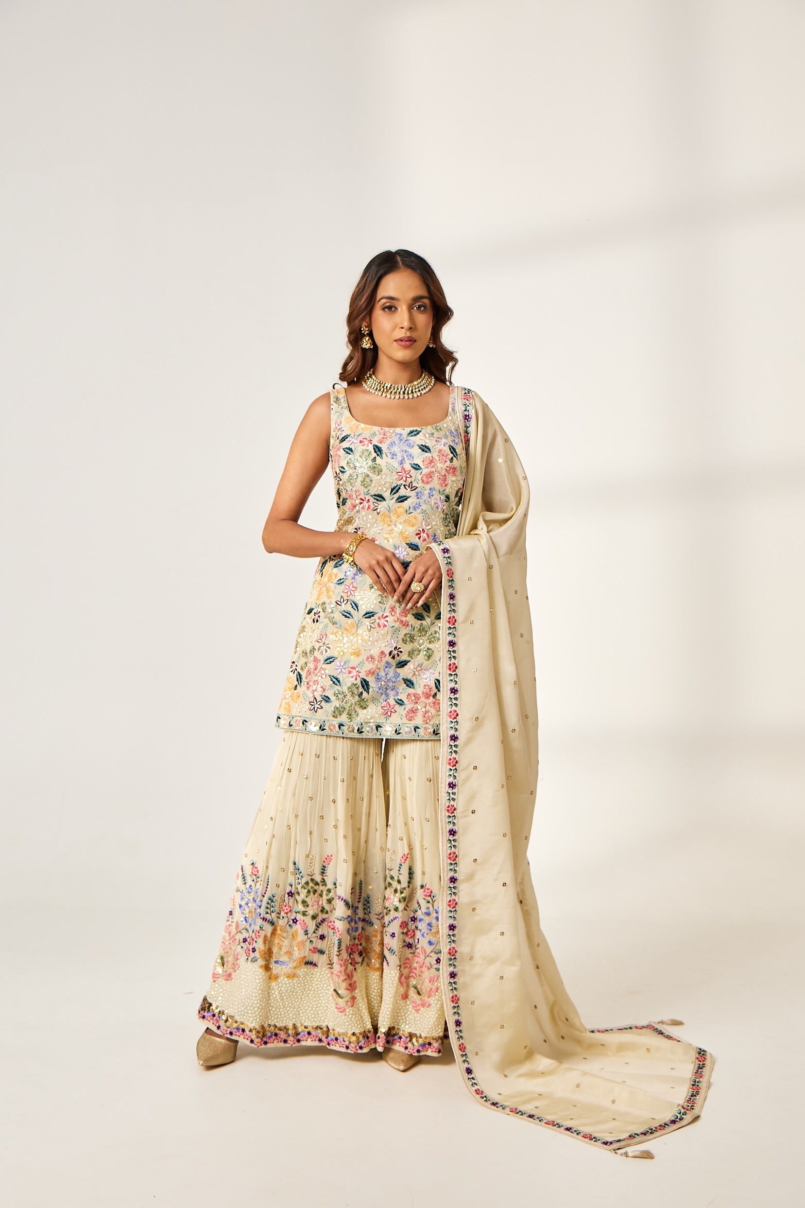 A woman poses in an ivory georgette co-ord set which includes a half-sleeve kurta and sharara pants with tikki embroidery.