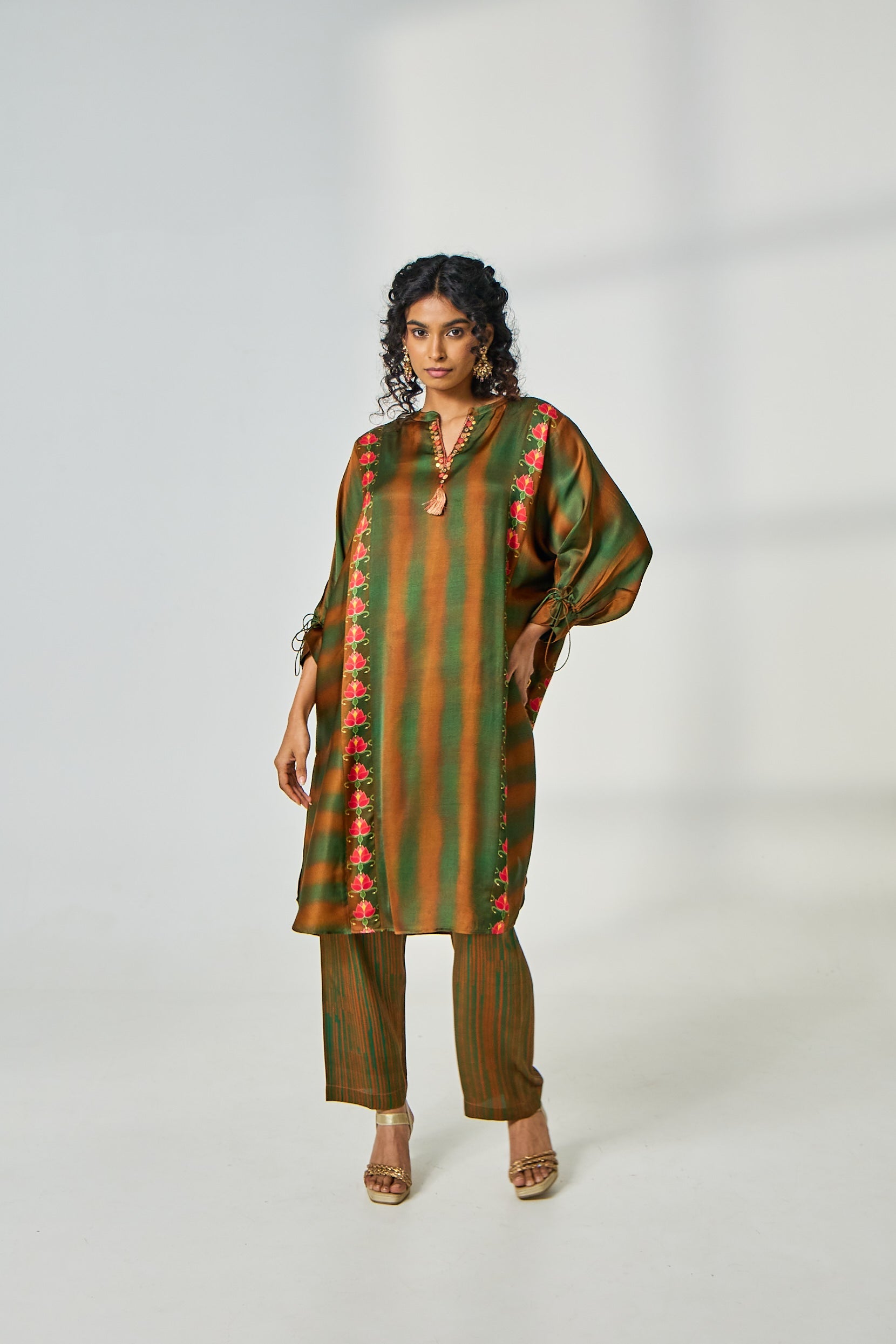 A woman poses in a satin co-ord set featuring a V-neck kurta with green and brown tie-dye, bead and metal work on the neckline, digital prints on both sides, and matching tie-dye pants.