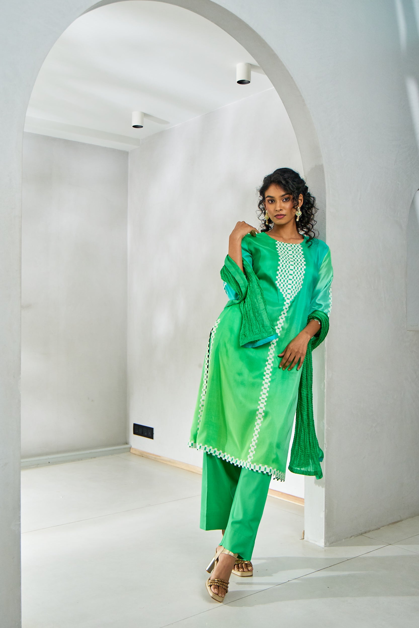 A woman poses in a lime green kurta set featuring a pure silk kurta with applique work on the neckline and sleeves, paired with cotton silk pants and a crushed silk dupatta.