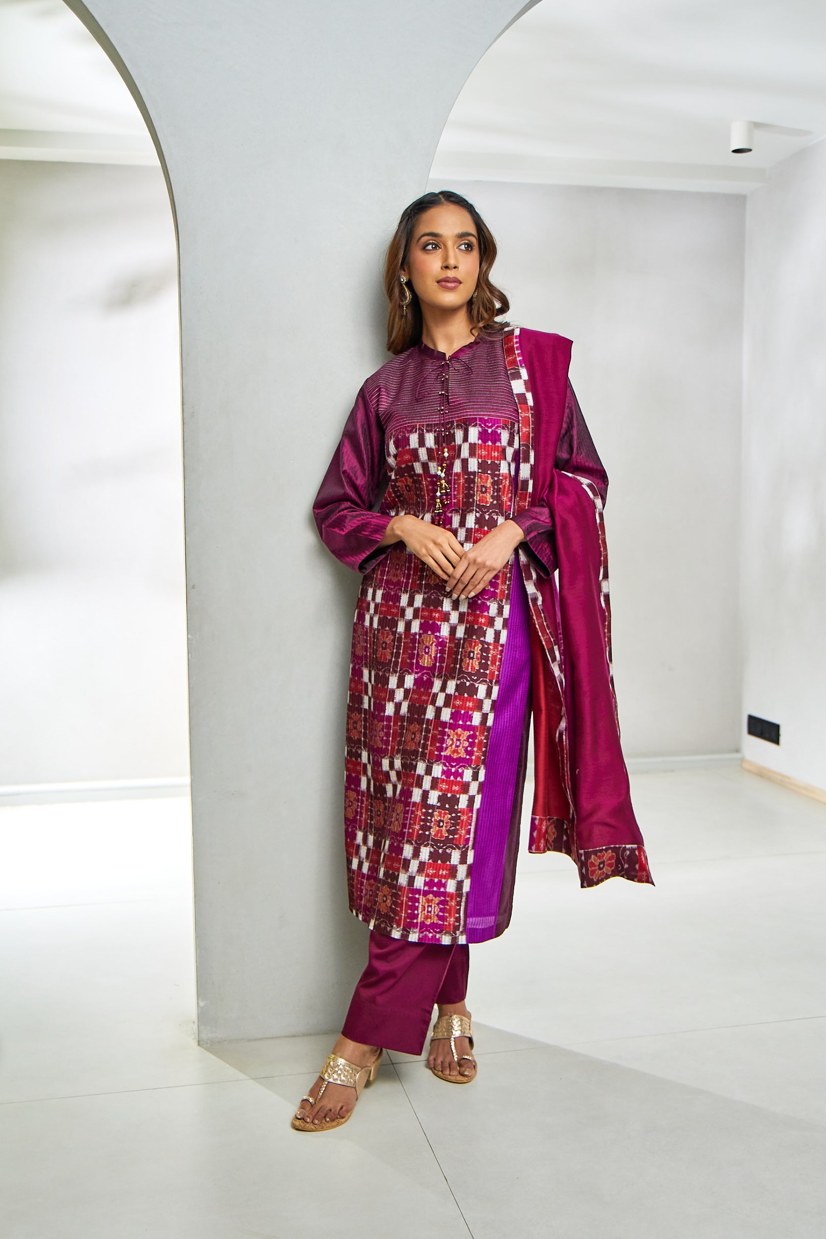 A woman poses in a traditional Ikat suit featuring a mandarin collar kurta crafted from handwoven cotton in earthy tones, adorned with classic geometric patterns, paired with straight-cut pants and a lightweight dupatta for an elegant, heritage-inspired look.