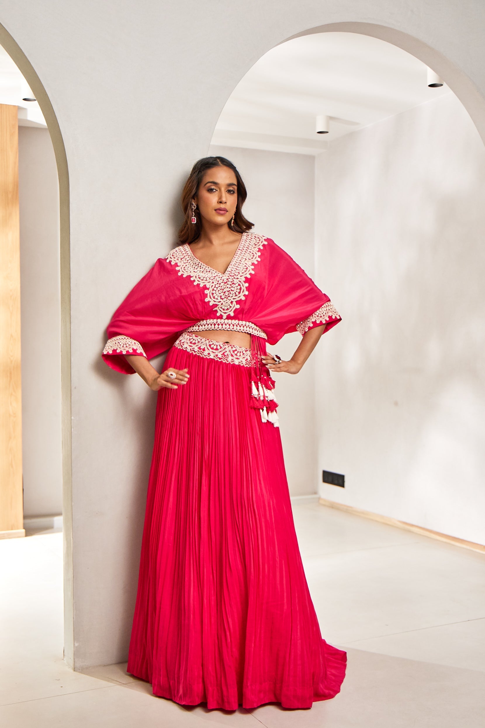 A woman dazzles in a hot pink crepe silk co-ord set featuring a crop top and skirt. Embellished with French knots, sequins, tassels, and pot workâ€â€designed for festive flair with a modern twist.