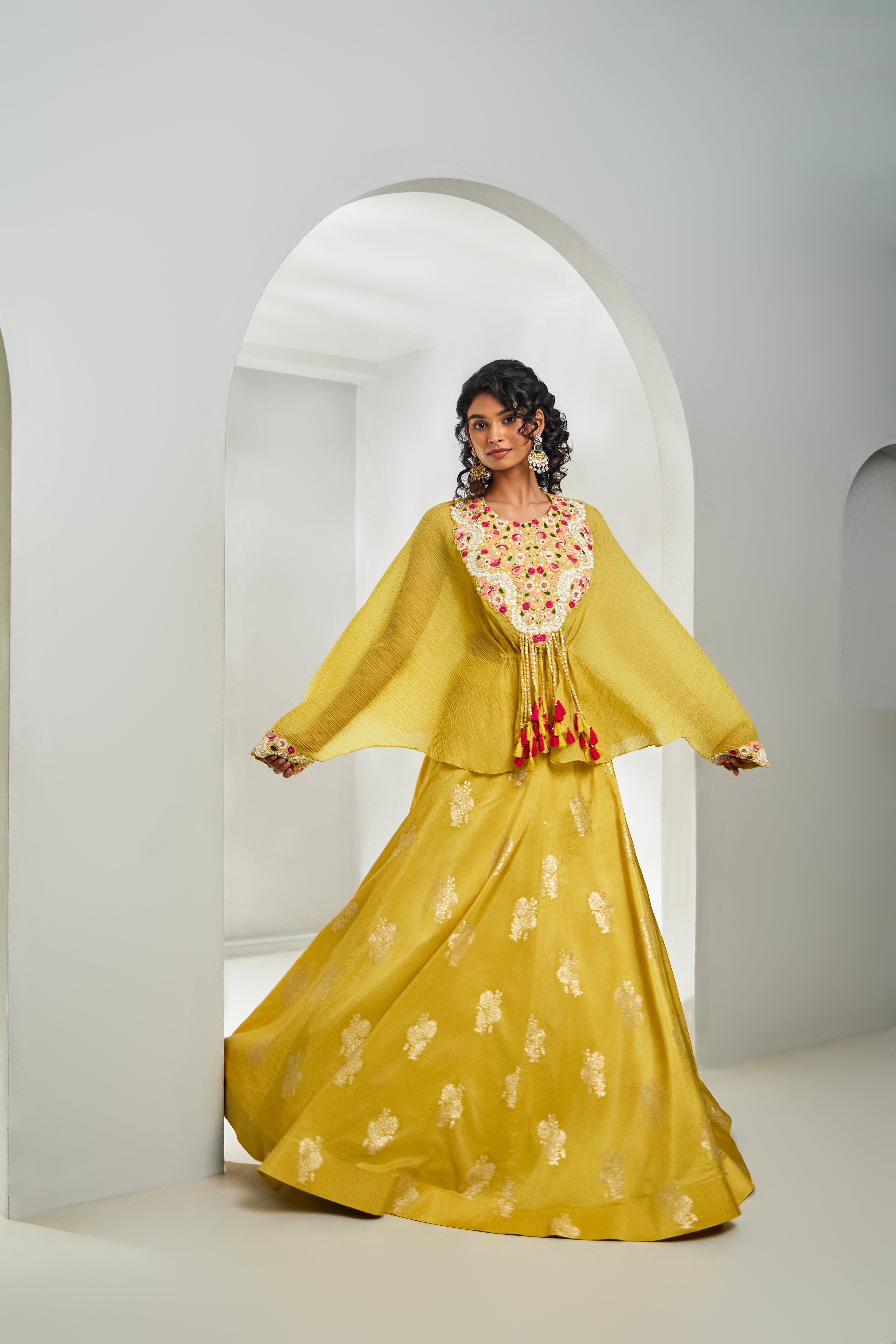 A woman stuns in a vibrant yellow Indo-Western set, featuring a chiffon kaftan-style top and silk ghagra. Adorned with multicolour thread, sequins, katdhana, and bead workâ€â€made for sunlit celebrations.