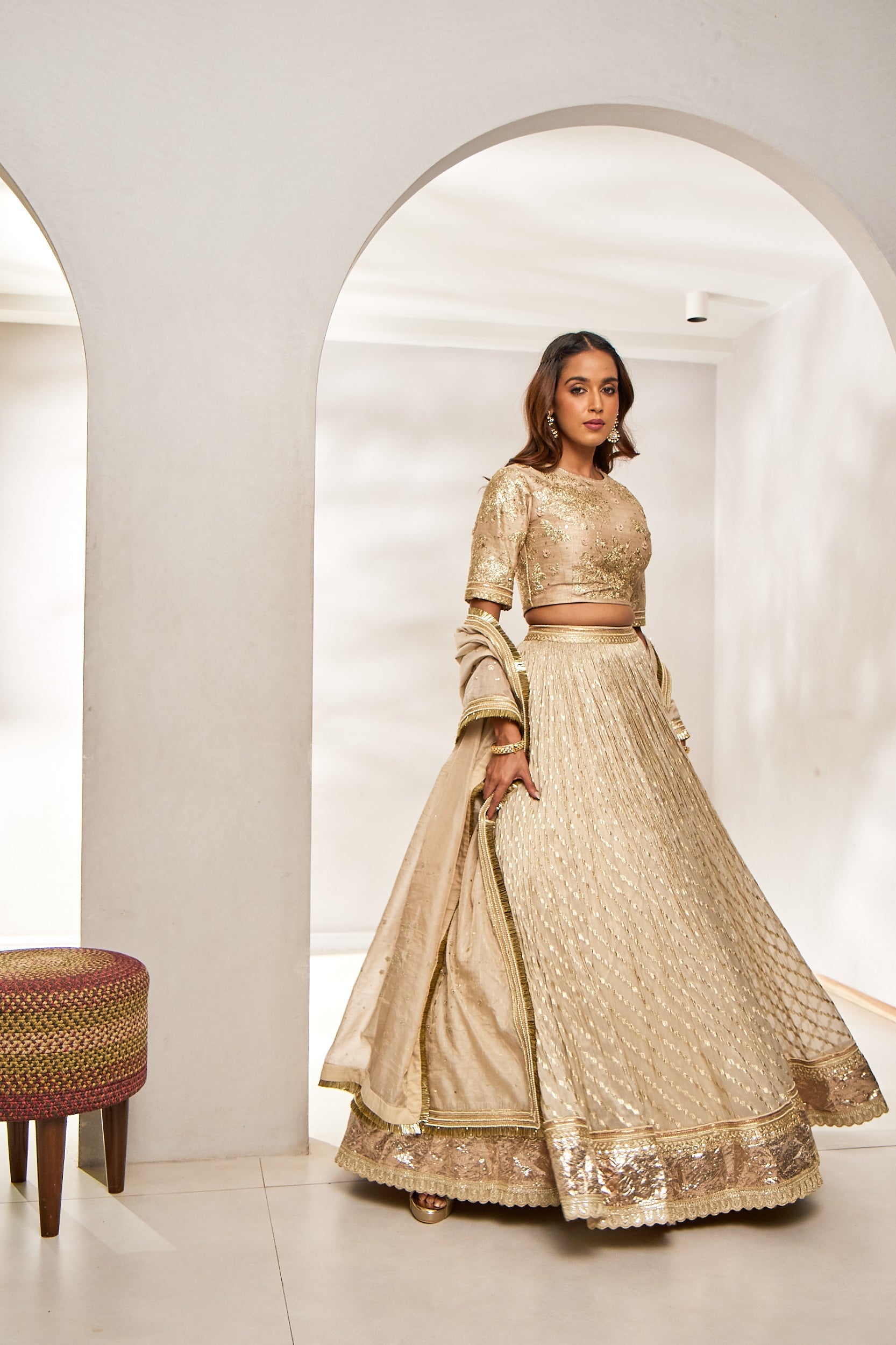 A woman glows in a beige wedding lehenga set, featuring a raw silk blouse, chanderi ghagra, and a tissue dupatta. The ensemble is detailed with katdana, sequin, and thread embroidery, finished with a lampi borderâ€â€ideal for a graceful bridesmaid look.