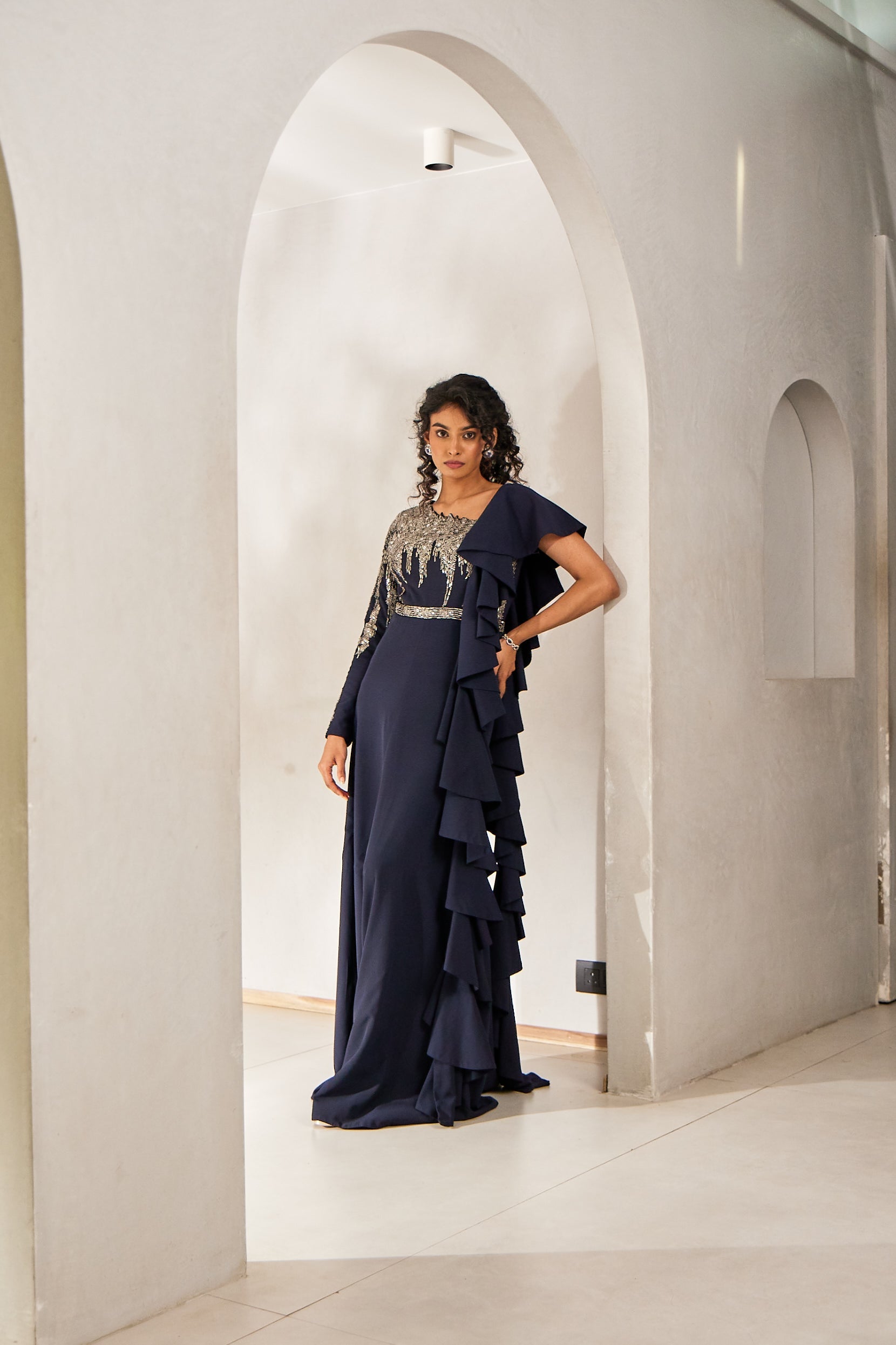 A woman exudes contemporary flair in a blue one-shoulder Indo-Western gown, crafted in crepe-georgette. Adorned with katdana, sequins, pot, and long tube bead workâ€â€made for elegant evening affairs.