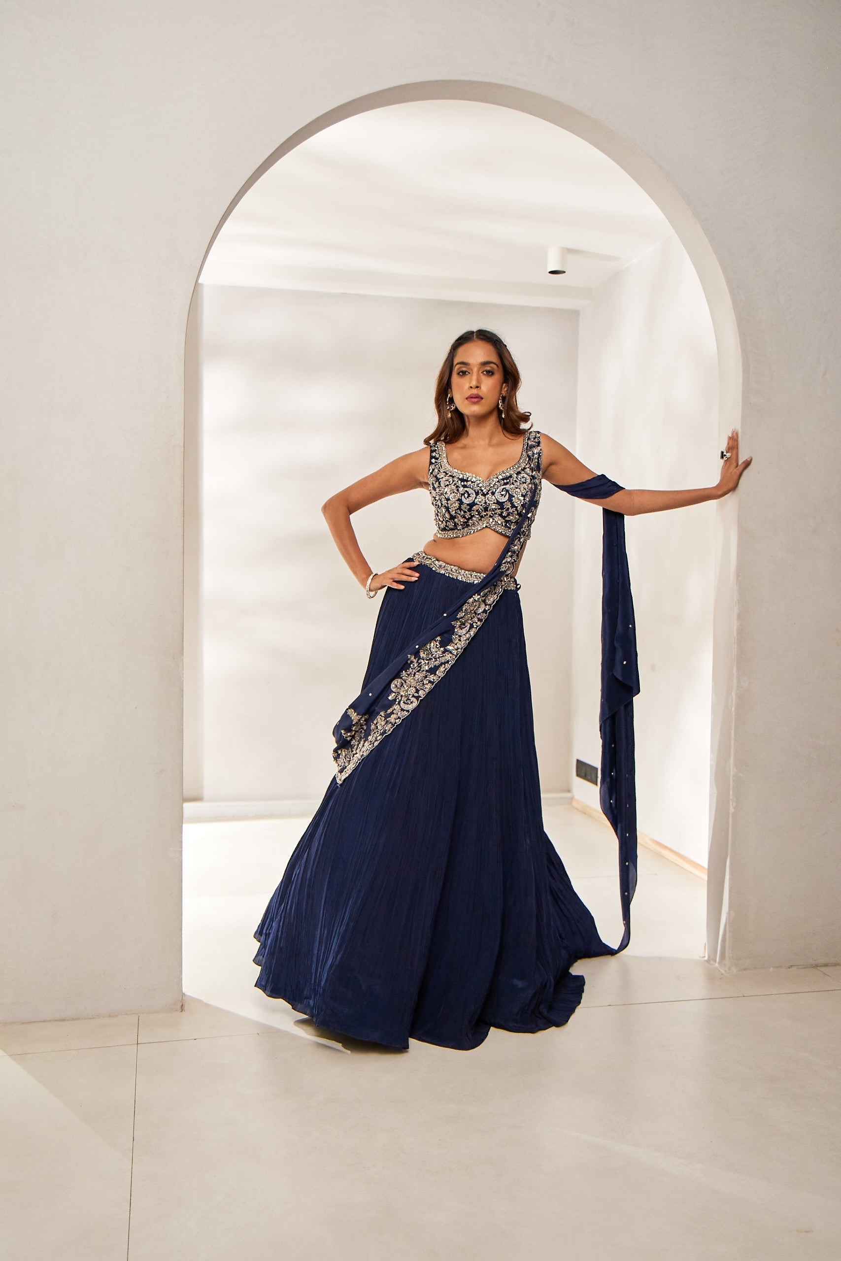 A woman stuns in a navy blue crepe silk draped ghagra saree set, featuring a blouse and an attached dupatta. The ensemble is embellished with zari, sequins, and intricate cutworkâ€â€blending tradition and trend for festive evenings.