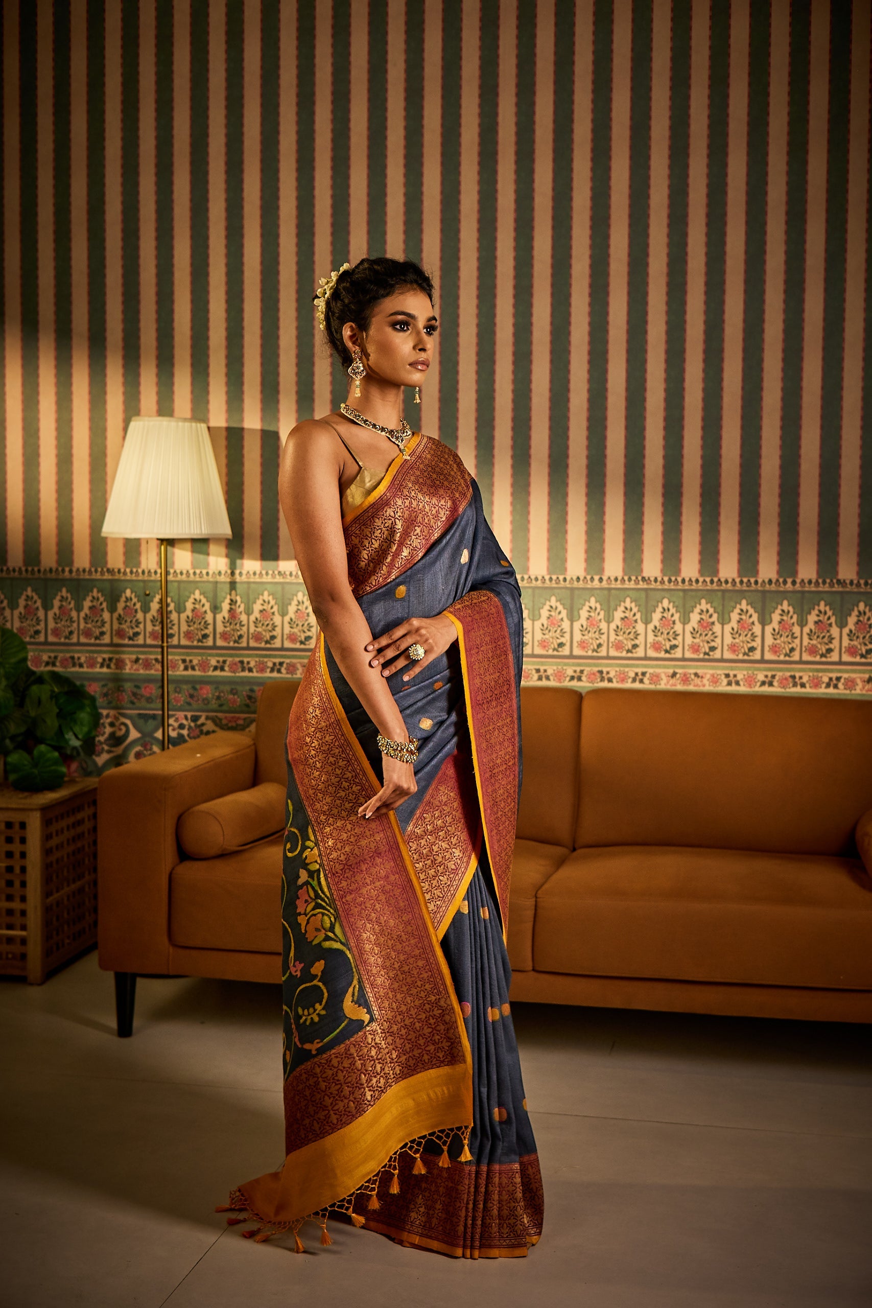 A woman poses in a grey tussar silk saree featuring pure handwoven motifs, zari-detailed borders, and a digitally printed pallu, styled with a matching blouse fabric and petticoat.