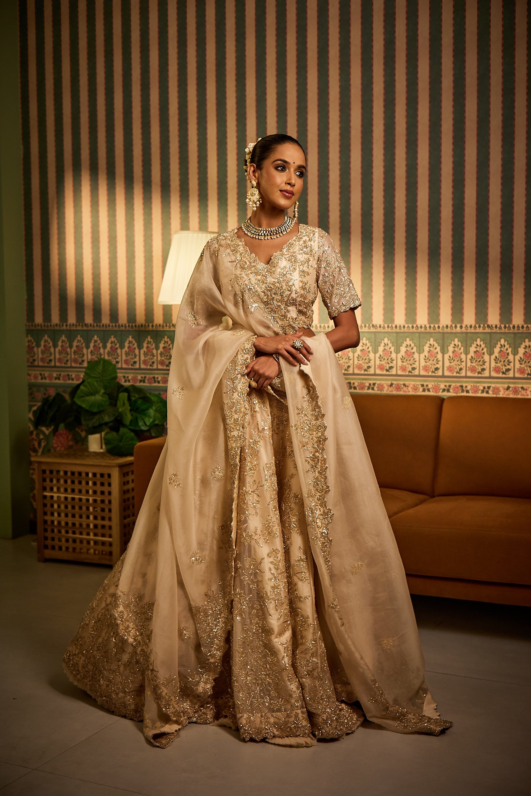 A woman radiates charm in an ivory and gold organza wedding lehenga set. Embellished with sequins, zari, katdana, and pearl work, the ensemble captures the essence of refined eleganceâ€â€perfect for a bridesmaid’s moment in the spotlight.
