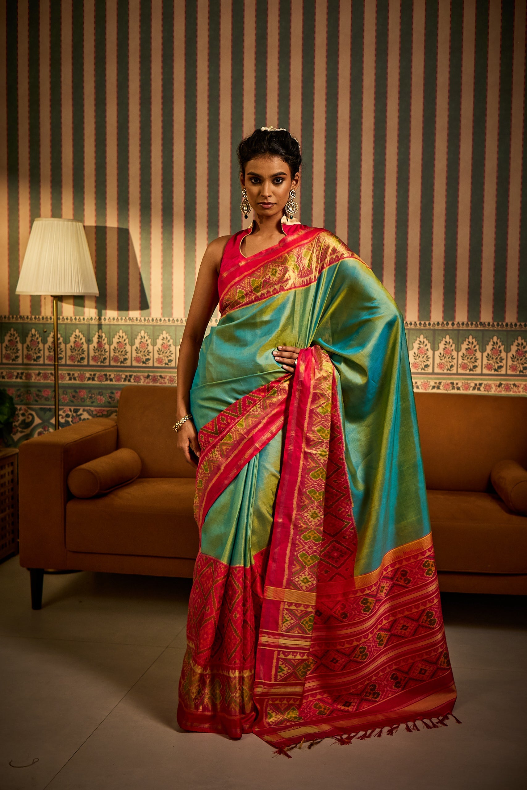 A woman poses in a pista green handloom silk saree featuring traditional handwoven patola patterns, finished with a striking contrast pink border and styled with a matching blouse fabric and petticoat.
