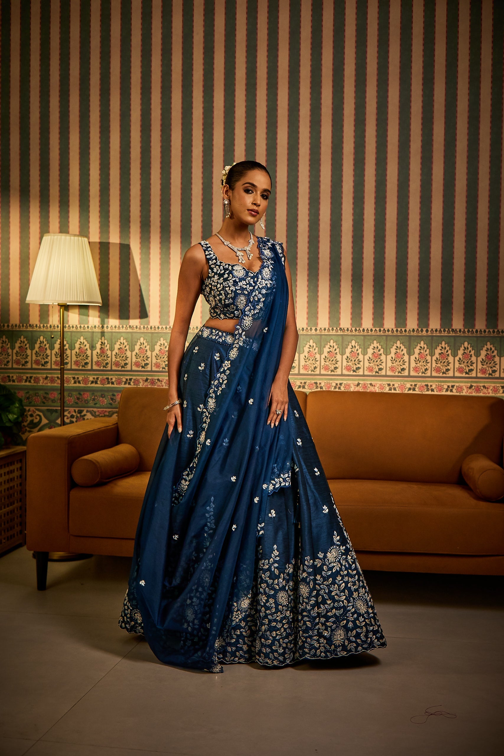 A woman dons a petrol blue silk ghagra choli set, paired with a sheer organza dupatta. The outfit is adorned with delicate thread, stone, and pearl embroideryâ€â€perfect for sangeet celebrations.