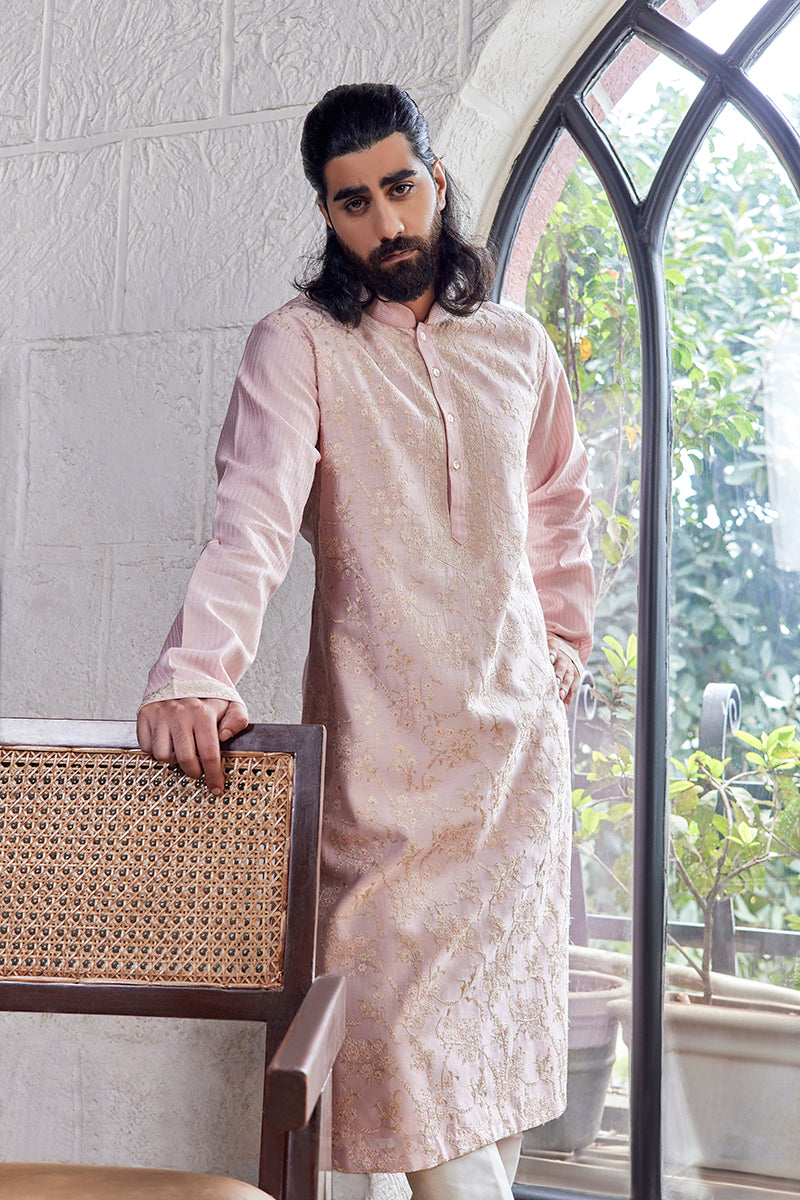 A man in a baby pink chanderi silk kurta set from BenzerWorld ethnicwear store poses in front of an arched window.