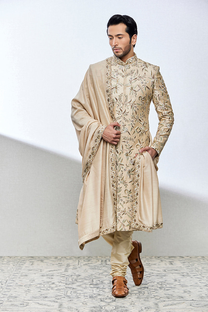 A man poses in a beige raw silk sherwani from BenzerWorld ethnicwear store.