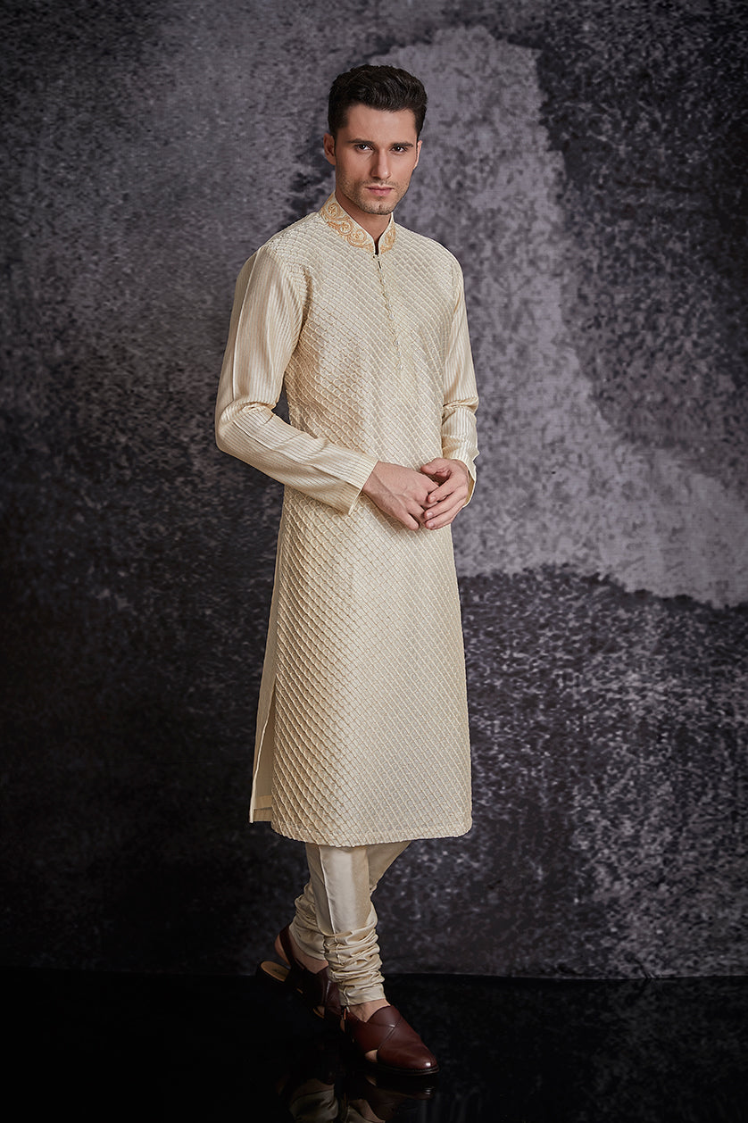 A man poses in a beige silk embroidered kurta set from BenzerWorld ethnicwear store.
