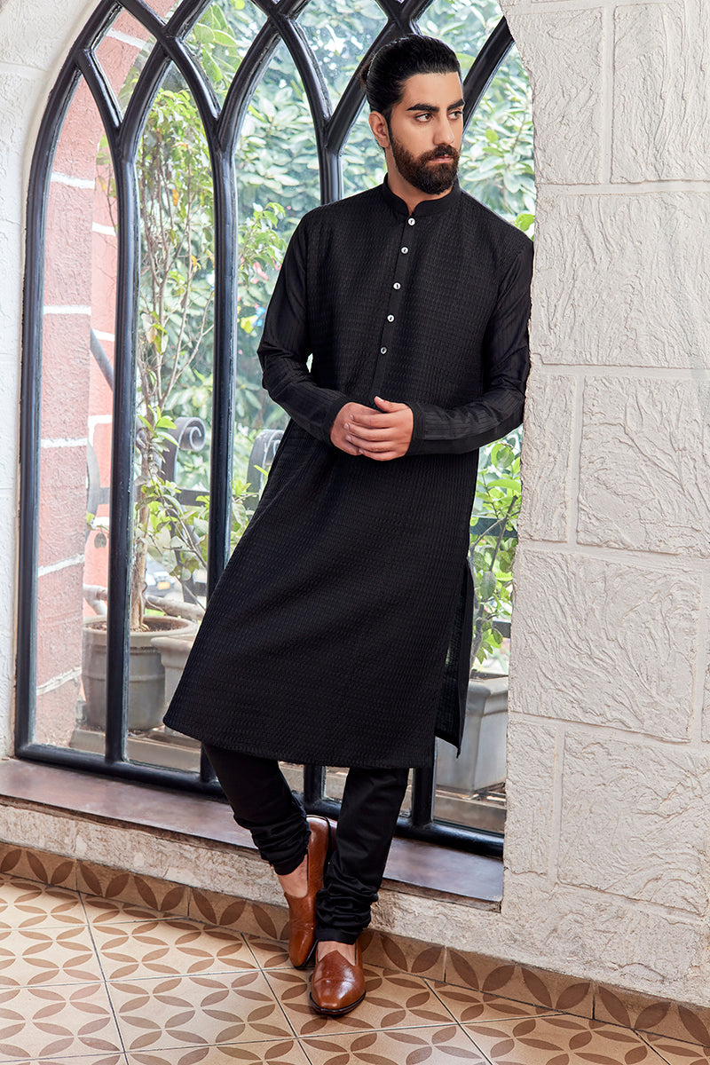 A man in a black cotton silk kurta set from BenzerWorld ethnicwear store poses in front of an arched window.