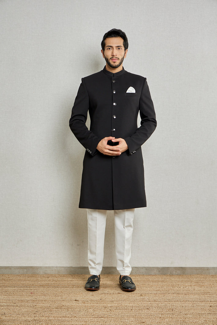 A man poses in a black jute Indo-Western suit from BenzerWorld ethnicwear store.