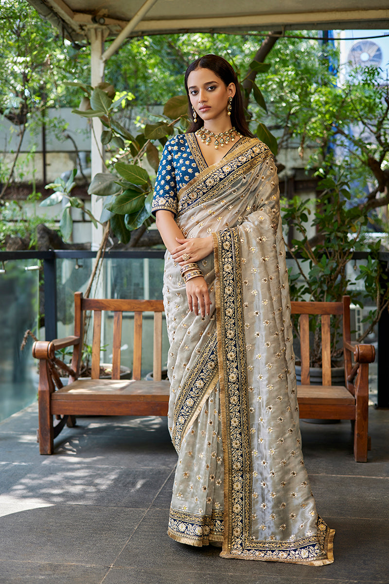 A woman poses in a blue-grey tissue organza saree from BenzerWorld ethnicwear store.