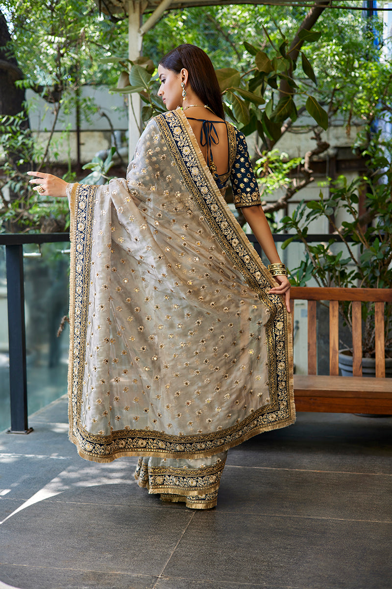 A woman poses in a blue-grey tissue organza saree from BenzerWorld ethnicwear store.
