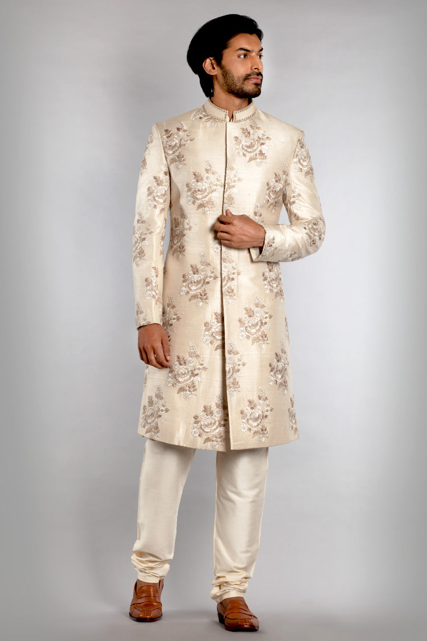 A man poses in a cream silk groom's sherwani from BenzerWorld ethnicwear store.