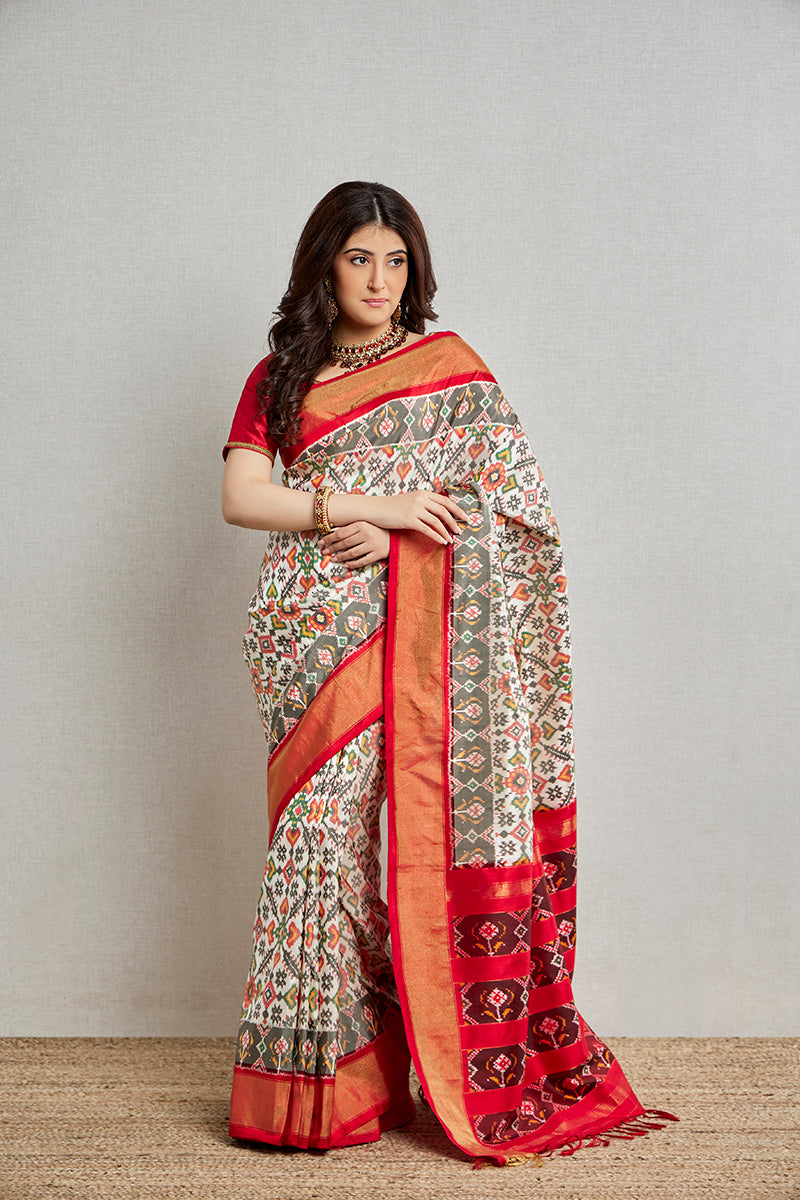 A woman poses in a cream silk patola saree with a blouse piece from BenzerWorld ethnicwear store, as she smiles.