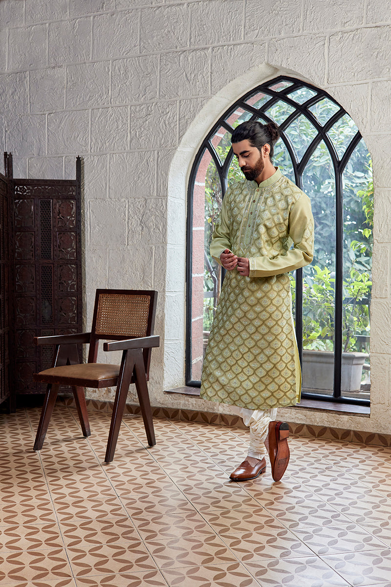 A man in a green chanderi silk kurta set from BenzerWorld ethnicwear store poses in front of an arched window.