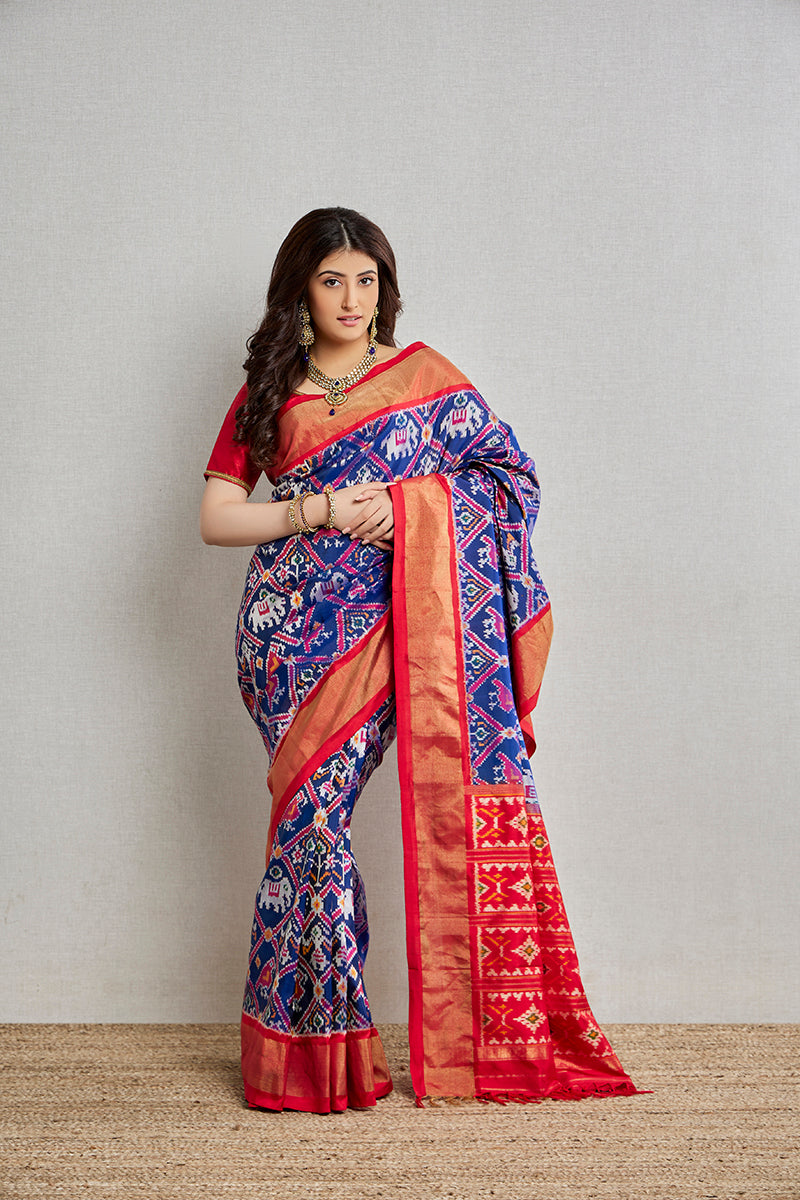 A woman poses in an indigo silk patola saree from BenzerWorld ethnicwear store, with her hands clasped in front of her waist.