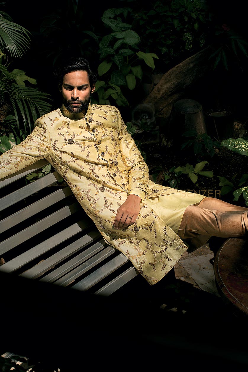 A man poses in a lemon yellow silk sherwani from BenzerWorld ethnicwear store.