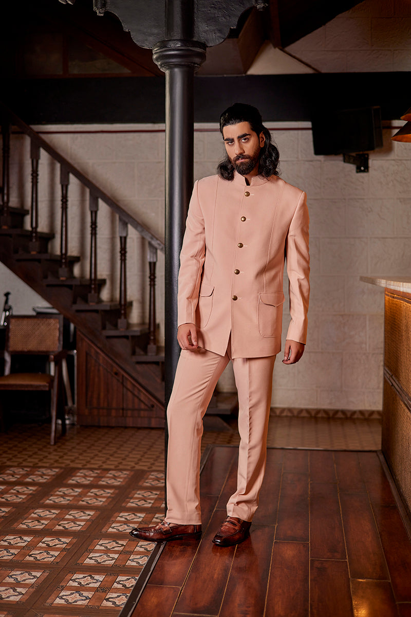 A man in a light peach terrywool suit from BenzerWorld ethnicwear store poses in front of pole.