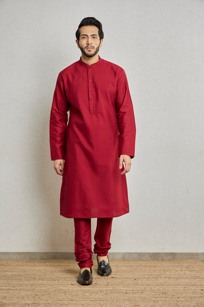 A man poses in a maroon cotton silk kurta set from BenzerWorld ethnicwear store while standing in front of a wall.