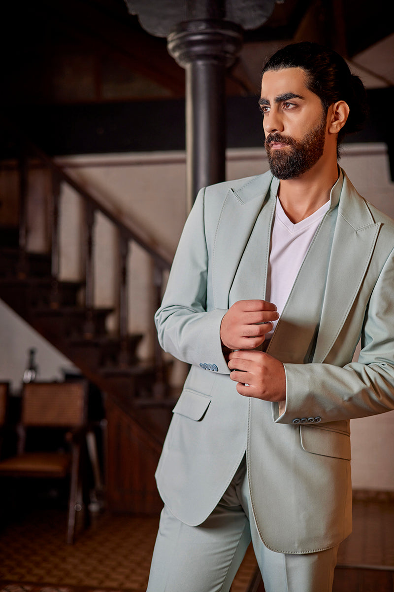 A man in a mint terrywool two-piece suit from BenzerWorld ethnicwear store poses in front of a pole.