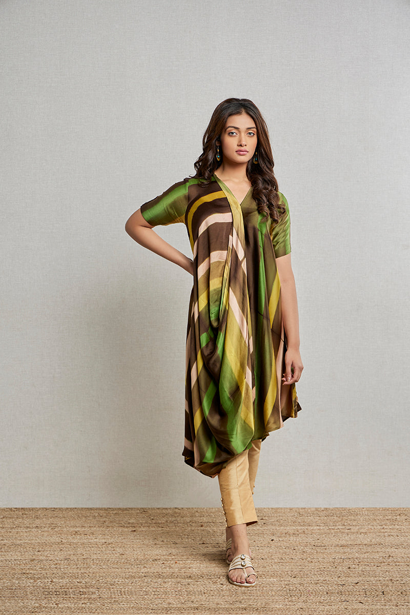 A woman poses in a green-blue satin silk short kurti from BenzerWorld ethnicwear store, while standing near a bench.