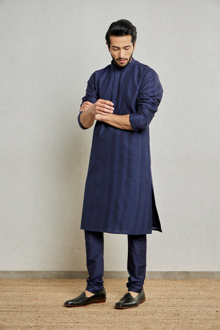 A man rolls up his sleeves while posing in a navy blue cotton silk kurta set from BenzerWorld ethnicwear store.