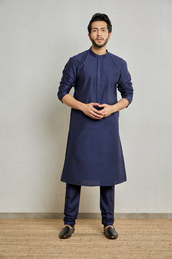 A man poses in a navy blue cotton silk kurta set from BenzerWorld ethnicwear store while standing in front of a wall.