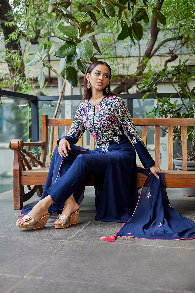 A woman poses in a navy blue georgette ladies suit from BenzerWorld ethnicwear store, while sitting down.