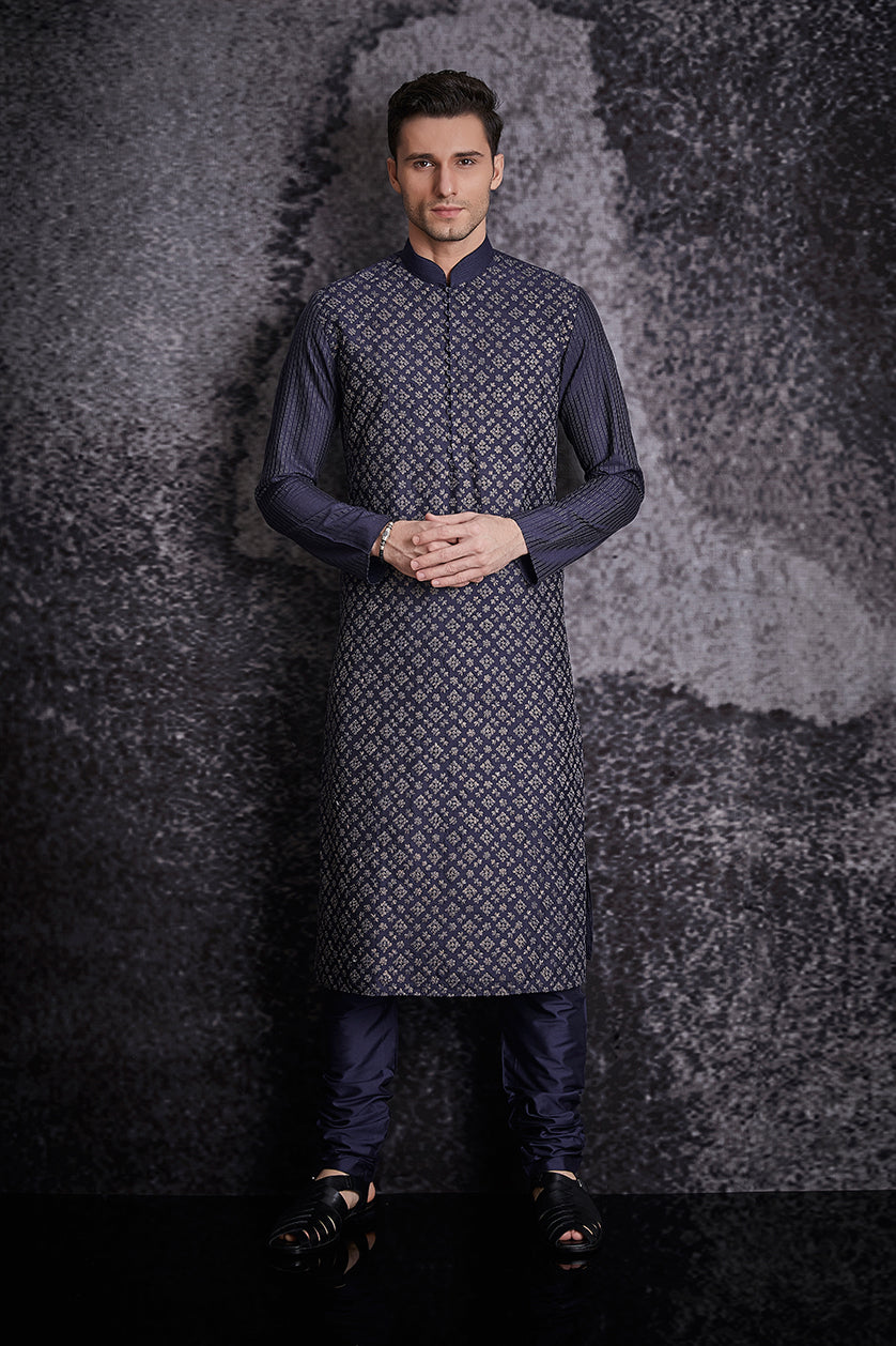 A man poses in a navy blue silk embroidered kurta set from BenzerWorld ethnicwear store.