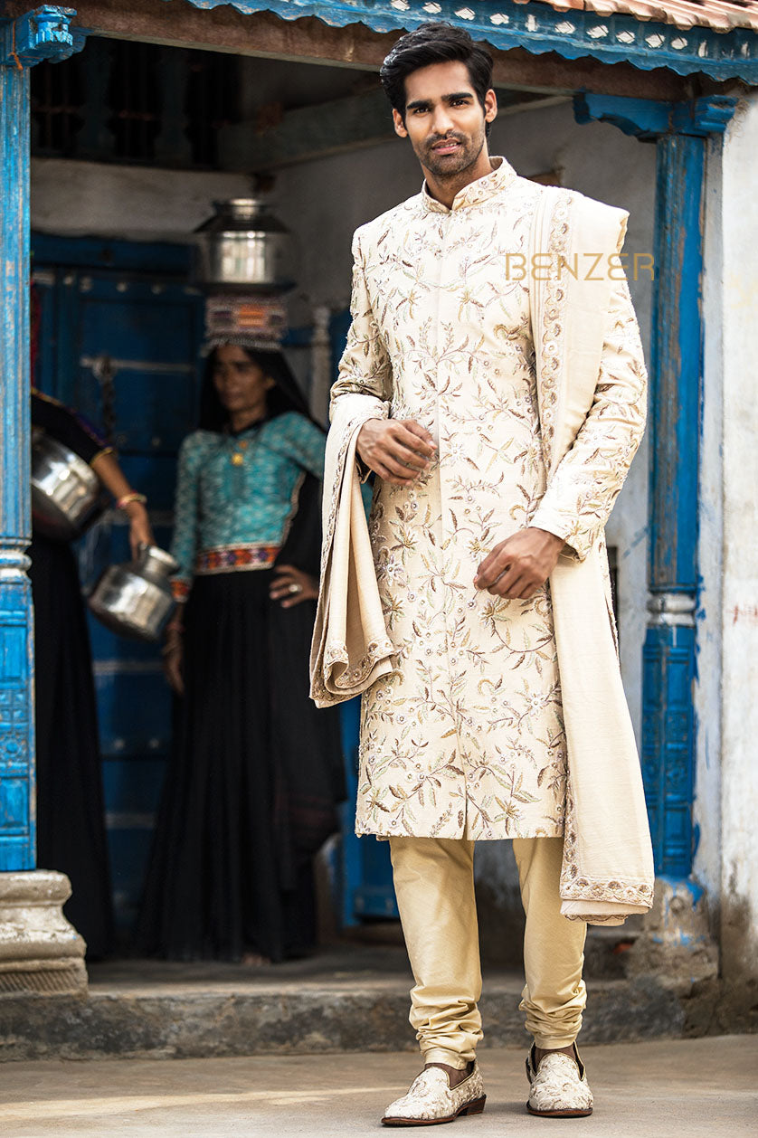 A man poses in a pearl white silk groom's sherwani from BenzerWorld ethnicwear store.