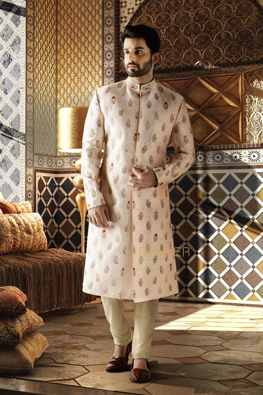 A man poses in a peach pink raw silk groom's sherwani from BenzerWorld ethnicwear store.