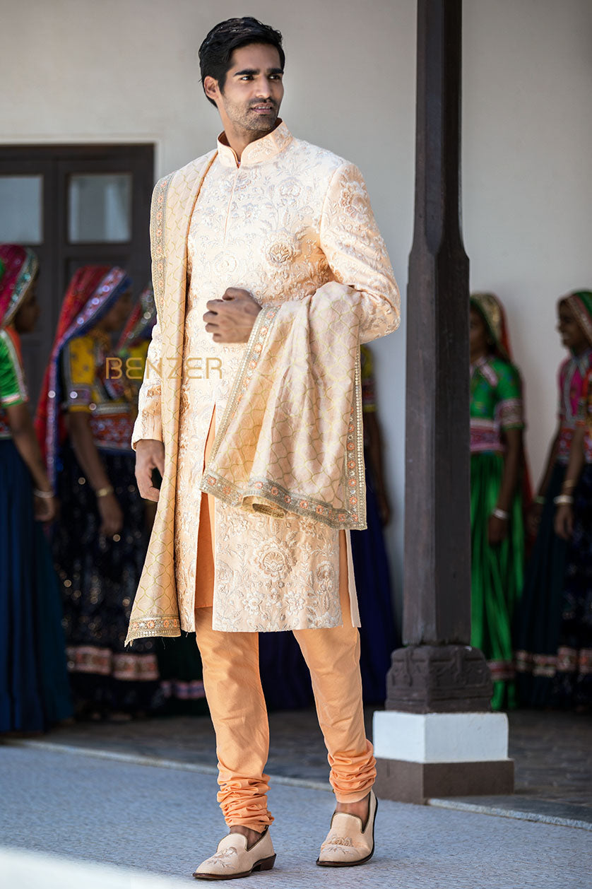 A man poses in a peach silk groom's sherwani from BenzerWorld ethnicwear store.