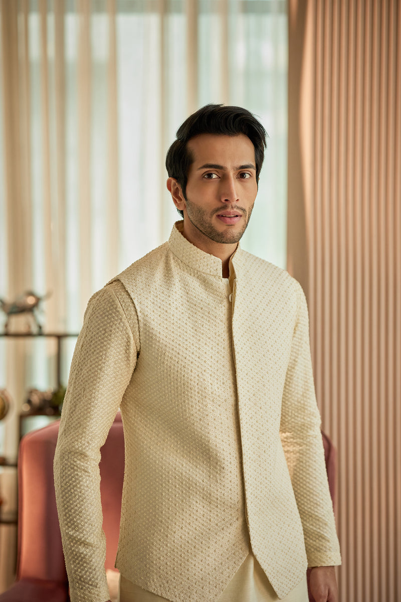 A man in a cream munga silk kurta and bundi set from BenzerWorld ethnicwear store poses with this top half in view.