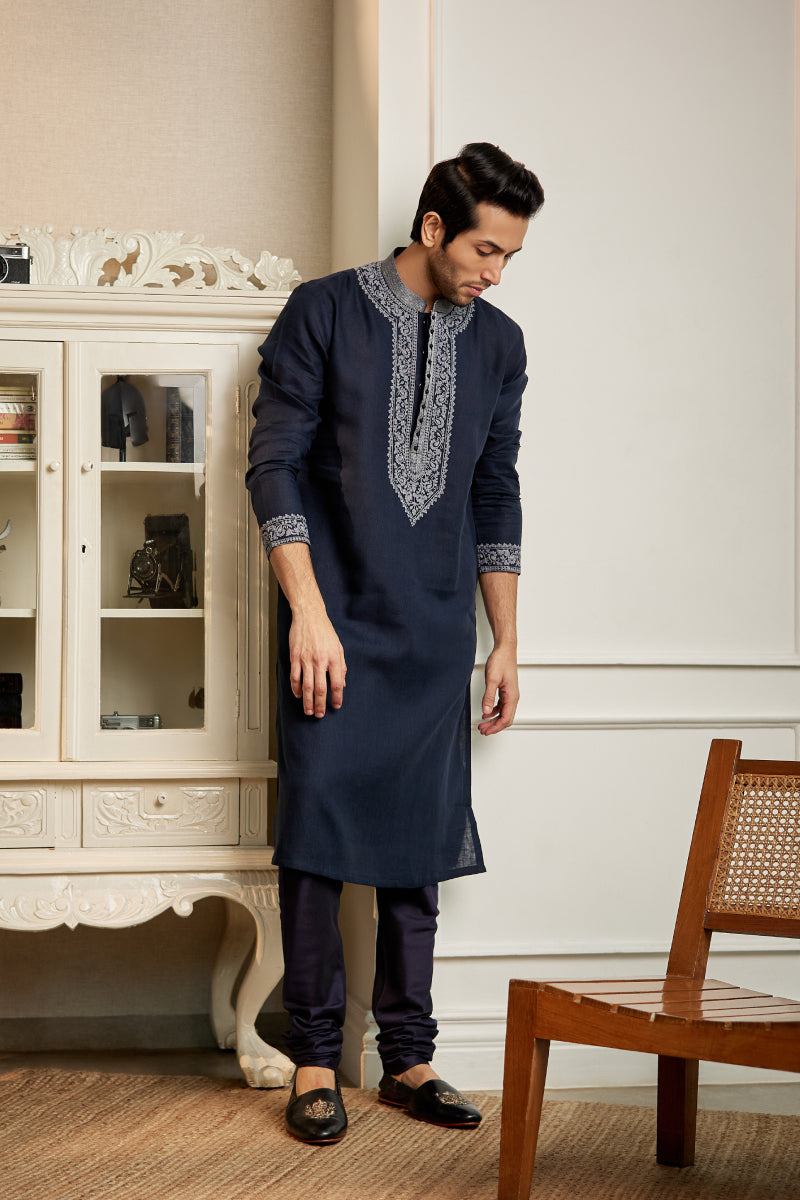 A man in a navy blue linen kurta set from BenzerWorld ethnicwear store looks down while posing for the camera.