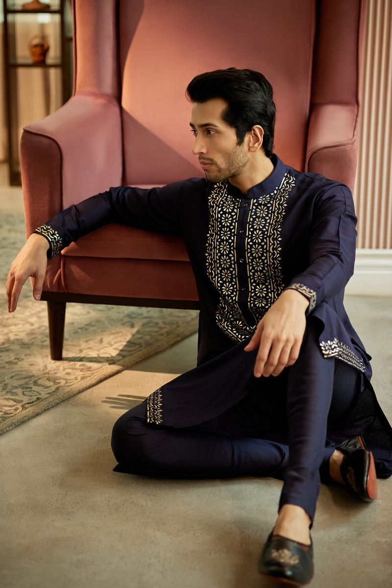 A man in a navy blue cotton silk kurta set from BenzerWorld ethnicwear store poses in a sitting position.