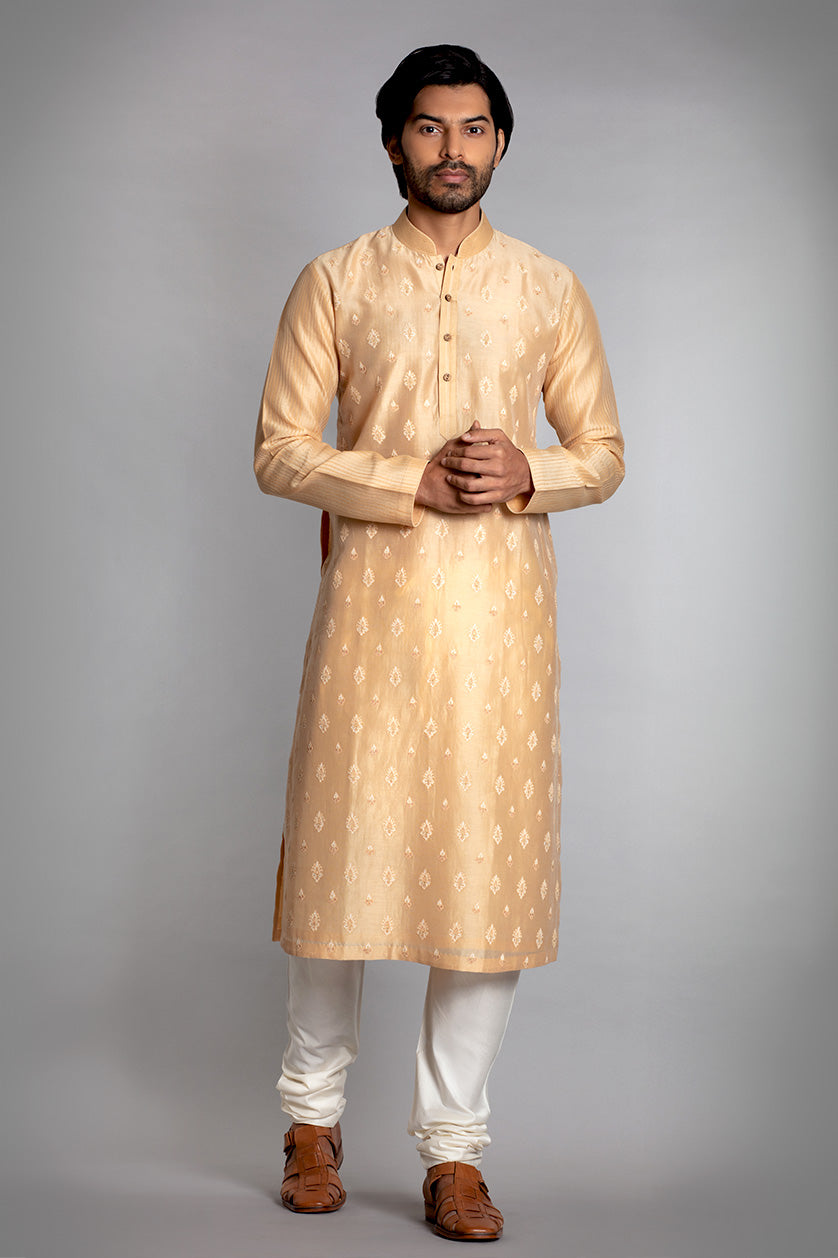 A man poses in a beige cotton silk embroidered kurta set from BenzerWorld ethnicwear store.
